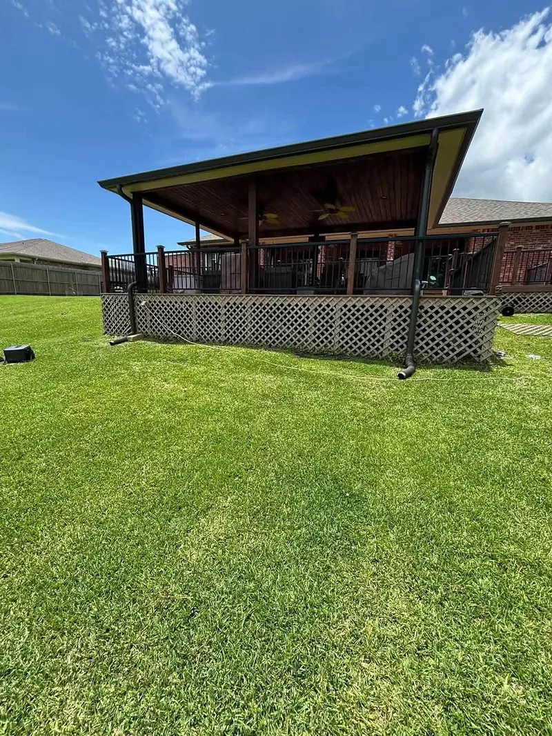 Covered backyard deck with black metal railing and new lattice skirting under a blue sky