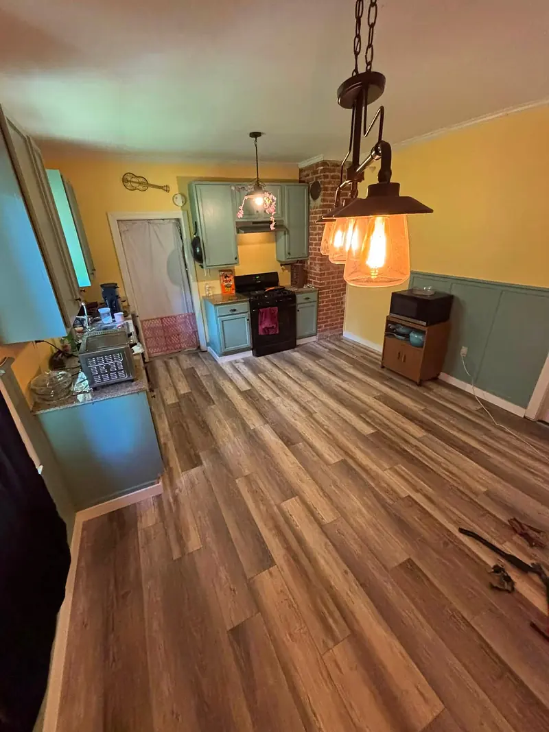Kitchen with newly installed wood-look plank flooring, teal cabinets and pendant lights