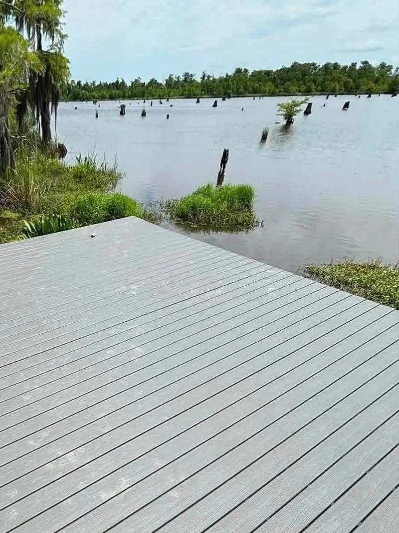 Finished gray composite deck boards at the edge of a cypress-lined lake