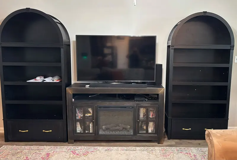 Black arched bookcases on either side of a media console with an electric fireplace