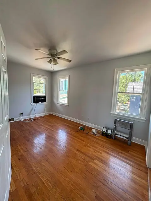 Empty bedroom with a glossy hardwood floor, white baseboards and three windows