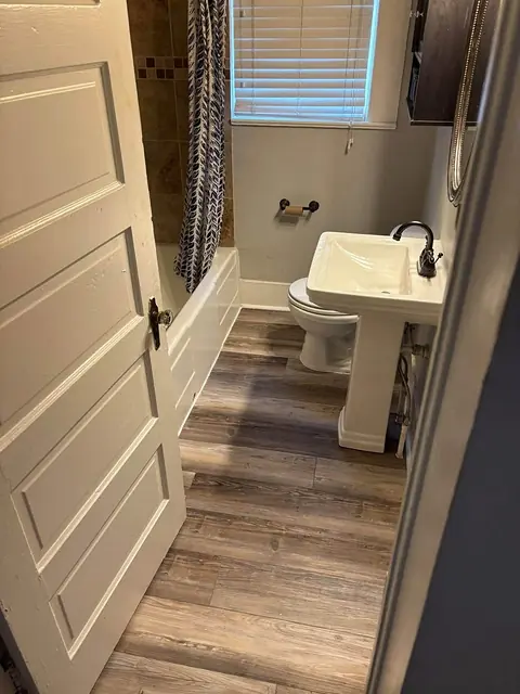 Doorway view of a bathroom with new plank flooring, tub and pedestal sink