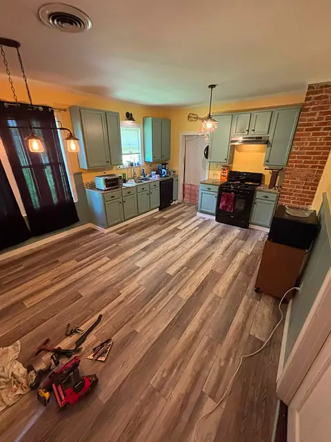 Wide view of a kitchen with new plank flooring, teal cabinets and an exposed brick chimney
