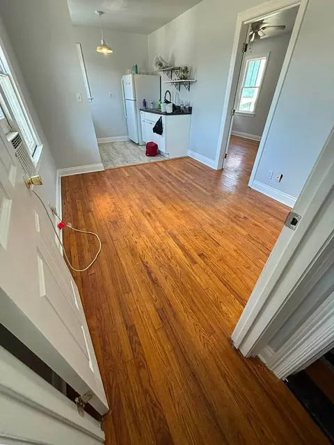 Hardwood floor hallway leading to a small kitchen, with white doors and trim