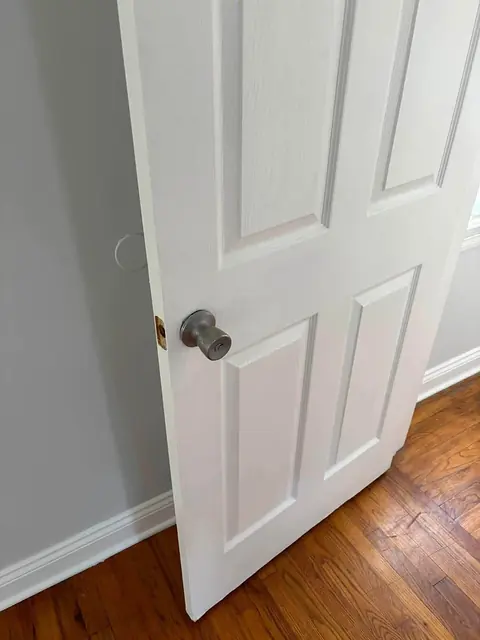 White six-panel interior door with a new knob, white baseboard and hardwood floor