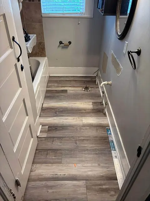 Narrow bathroom with new wood-look plank flooring installed before the fixtures go back in
