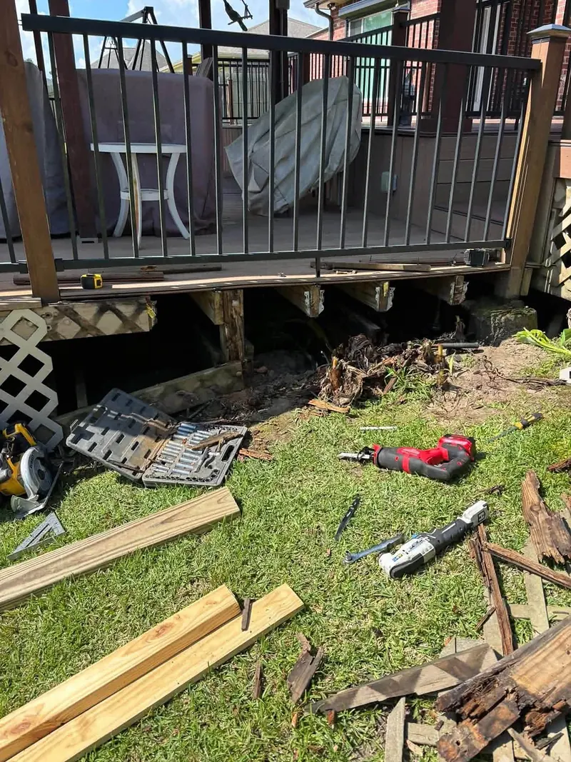 Rotted deck framing removed below a railing, with new lumber and tools on the lawn