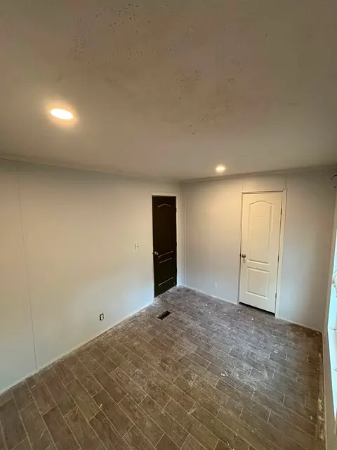 Room with a wood-look tile floor, one dark door and one white door