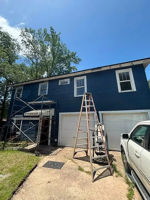 Two-story navy blue house with white trim, with scaffolding and a ladder set up for exterior work