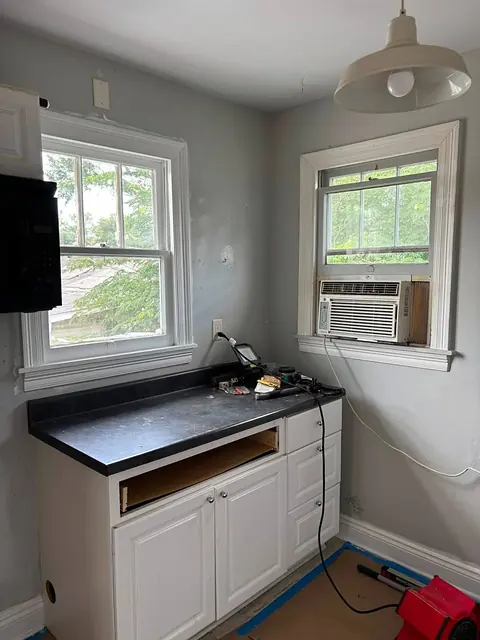 Small kitchen corner with white cabinets, dark countertop and trimmed windows during renovation