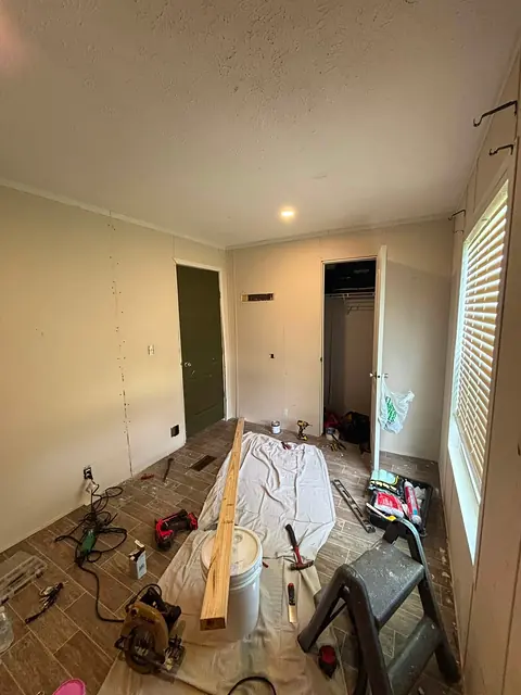Room midway through a wood-look tile floor installation, with tools on a drop cloth