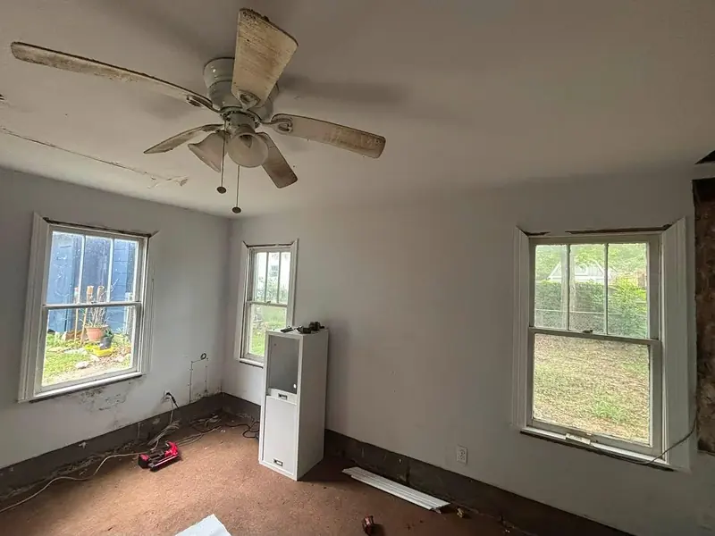 Empty room with a worn floor and three windows before renovation